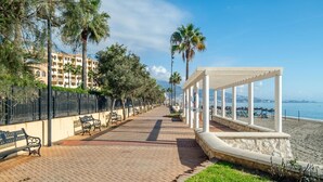 Un paseo marítimo con bancos, un corredor cubierto y vistas a la playa.