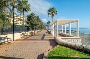 A seaside promenade with benches, a covered walkway, and a beach view.