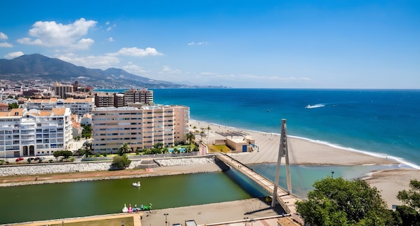 A coastal cityscape with a prominent cable-stayed bridge, a beach, and a marina.