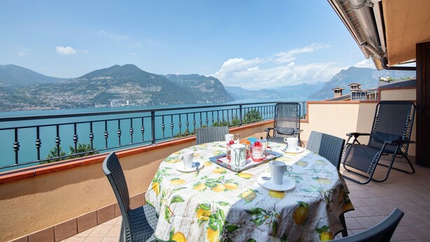 A balcony with a table set for two, overlooking a body of water and mountains.