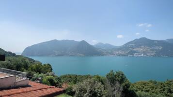 A view of a lake with mountains in the background, a building with a red roof, and a fence.