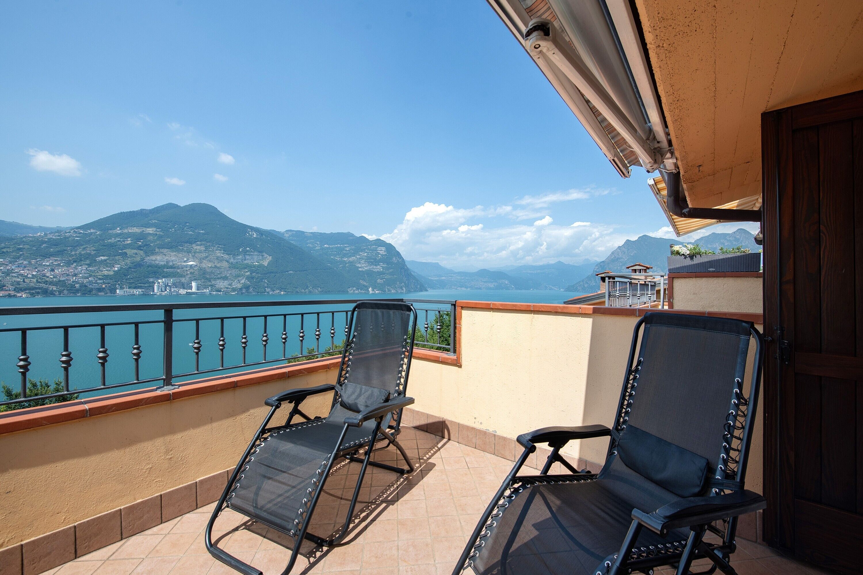 Ein Balkon mit zwei Stühlen, Blick auf einen See und Berge in der Ferne.