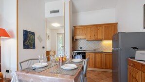 A dining area with a table set for four, a kitchen with wooden cabinets and a refrigerator, and a tiled backsplash.