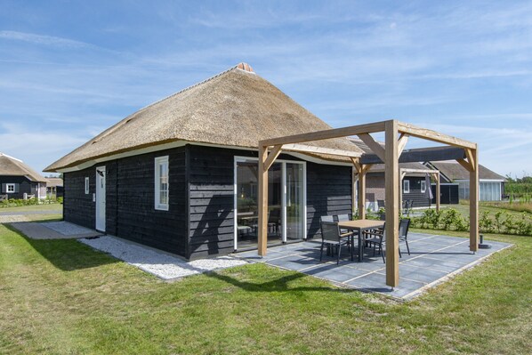 Une maison à toit de chaume, dotée d’un patio couvert et d’une pergola en bois.