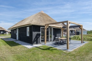 A thatched-roof house with a covered patio and outdoor seating. - Villa in Someren Near Golf Course (Someren)
