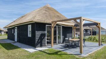 Cozy cottage with a covered outdoor seating area under a pergola, surrounded by a well-maintained lawn and patio.