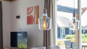 A dining area with a wooden table, chairs, and pendant lights with exposed bulbs. - Villa in Someren Near Golf Course (Someren)