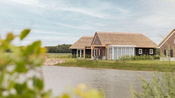 A row of traditional houses with thatched roofs, a wooden porch, and a view of a calm body of water. - Villa in Someren Near Golf Course (Someren)