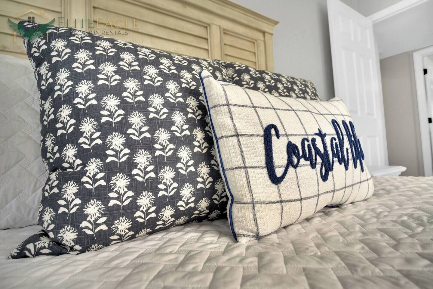 A bed with two decorative pillows, one with a floral pattern and the other with a grid and text.