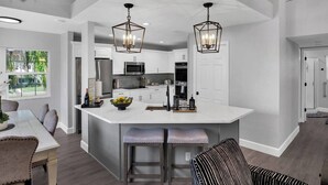 A modern kitchen with white cabinetry, a central island with bar stools, and pendant lighting. - Luxury 4BR Beach House on the Sand (Redington Beach)