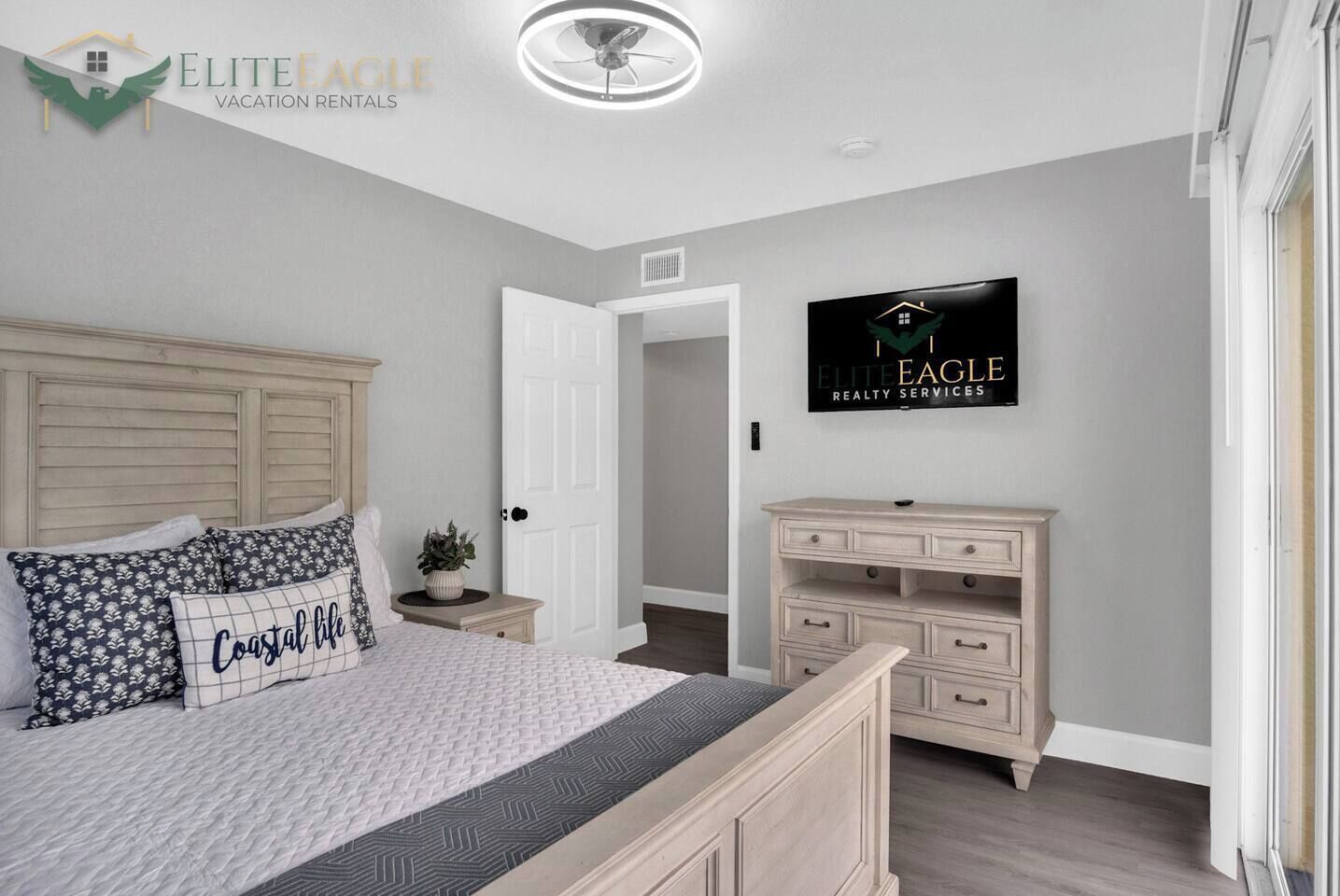 A bedroom with a bed, a nightstand, a dresser, a TV, and a door to another room.