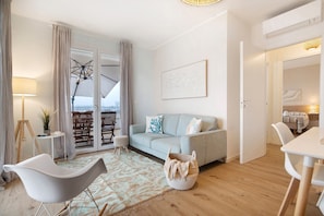 Un salon moderne avec un canapé, une table à manger, une lampe et une vue à travers une porte vitrée.