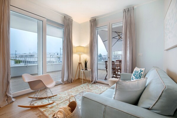 Un salon moderne avec un canapé, un fauteuil à bascule, une petite table avec une lampe et une vue dégagée grâce à de grandes fenêtres.