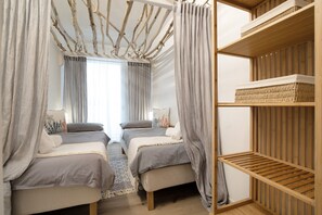 Une chambre avec deux lits, une étagère en bois et une fenêtre avec des rideaux.
