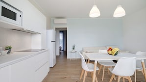 A modern kitchen with white cabinetry, a microwave, and a dining area with a white table and chairs. - Apartment 'Deluxe 5' with Shared Garden, Wi-Fi and Air Conditioning (Jesolo)