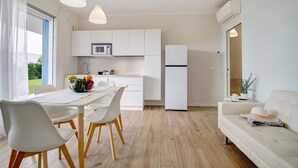 A modern kitchen with white cabinets, a dining table with chairs, a refrigerator, and an air conditioning unit. - Apartment 'Deluxe 5' with Shared Garden, Wi-Fi and Air Conditioning (Jesolo)