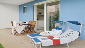 A sun lounger with a towel, a table with chairs, and a view of the kitchen through a glass door. - Apartment 'Deluxe 5' with Shared Garden, Wi-Fi and Air Conditioning (Jesolo)
