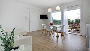 A modern living room with a sofa, dining table, chairs, a TV, and a balcony with outdoor furniture. - Apartment 'Deluxe 5' with Shared Garden, Wi-Fi and Air Conditioning (Jesolo)