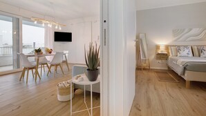 Un salon moderne avec un canapé, un coin repas comprenant une table et des chaises, une plante en pot et un téléviseur fixé au mur.
