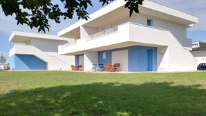 Un bâtiment moderne à deux étages, doté d’un toit plat, d’une porte bleue et d’un petit balcon agrémenté de mobilier d’extérieur.