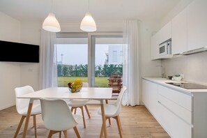 A modern kitchen with white cabinetry, a dining area with a white table and chairs, and a large window with a view of greenery. - Apartment 'Deluxe 6' with Shared Garden, Wi-Fi and Air Conditioning (Jesolo)