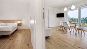 Ein modernes Hotelzimmer mit Bett, Essecke mit Tisch und Stühlen, einem an der Wand montierten Fernseher und großen Fenstern.