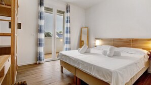 Une chambre à coucher avec un lit, un plancher en bois, une porte-fenêtre coulissante et un miroir.