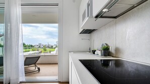 Une cuisine moderne avec un plan de travail noir, une fenêtre donnant sur l’extérieur et un balcon avec une chaise.