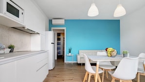 Une cuisine moderne avec des meubles blancs, un four à micro-ondes et un coin repas comprenant une table et des chaises blanches.