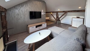 Een moderne loft slaapkamer met dakraam, een grote televisie, een bank en een klein tafeltje.