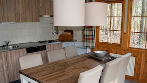 A modern kitchen with wooden cabinets, a white countertop, and a dining table with chairs. - Cozy Chalet With a Decorative Fireplace (Ruinen)