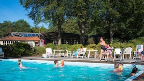 A swimming pool with people in the water, surrounded by lounge chairs and a building with a tiled roof. - Cozy Chalet With a Decorative Fireplace (Ruinen)