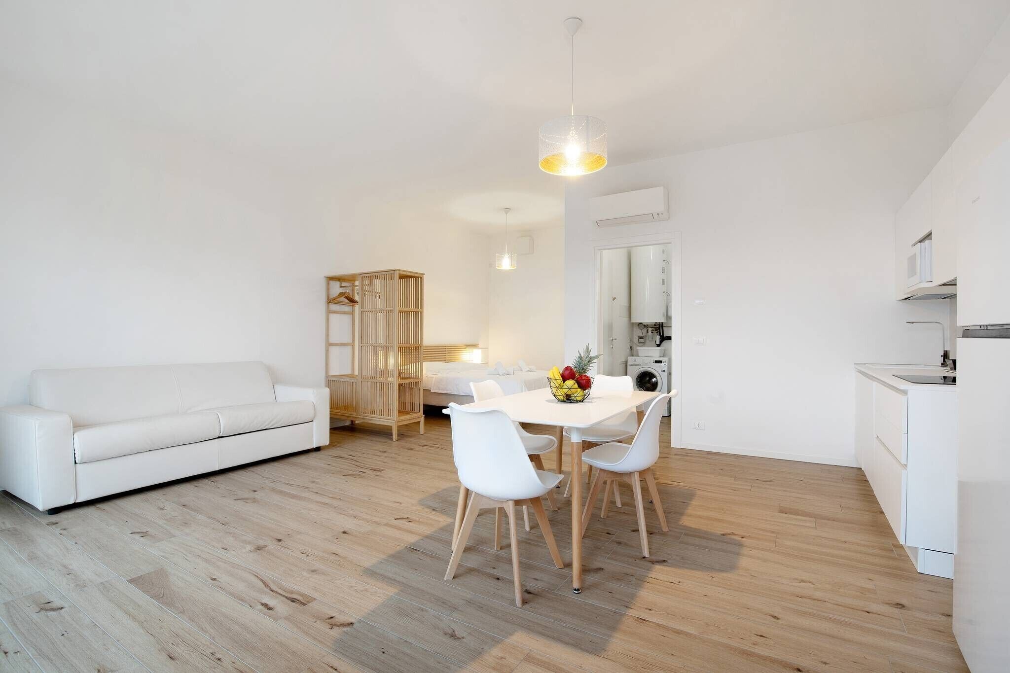 Un salon moderne avec un canapé blanc, une table à manger avec des chaises et un coin cuisine équipé d’appareils électroménagers.