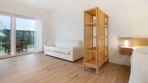 A modern living room with a white sofa, a wooden bookshelf, and a sliding glass door leading to an outdoor area. - Studio Apartment 'Open Space 2' with Shared Garden, Wi-Fi and Air Conditioning (Jesolo)