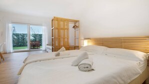 A bedroom with a large bed, a wooden headboard, a sliding glass door leading to an outdoor area, and a white curtain. - Studio Apartment 'Open Space 2' with Shared Garden, Wi-Fi and Air Conditioning (Jesolo)