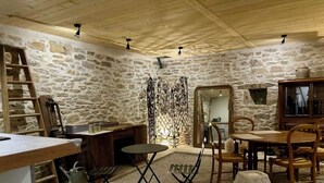 Habitació rústica amb parets de pedra, sostre de fusta, una taula de dinar amb caires, una escala i una taula petita amb una testosseta.