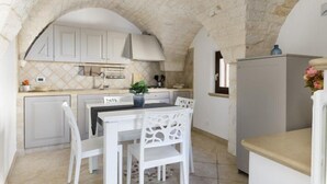 Een keuken met witte kastjes, een gewelfd plafond van steen, en een eethoek met witte stoelen en een tafel.