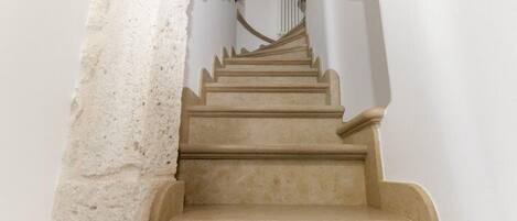 A staircase with a stone wall on one side and a white wall on the other, leading to a landing with a light fixture.