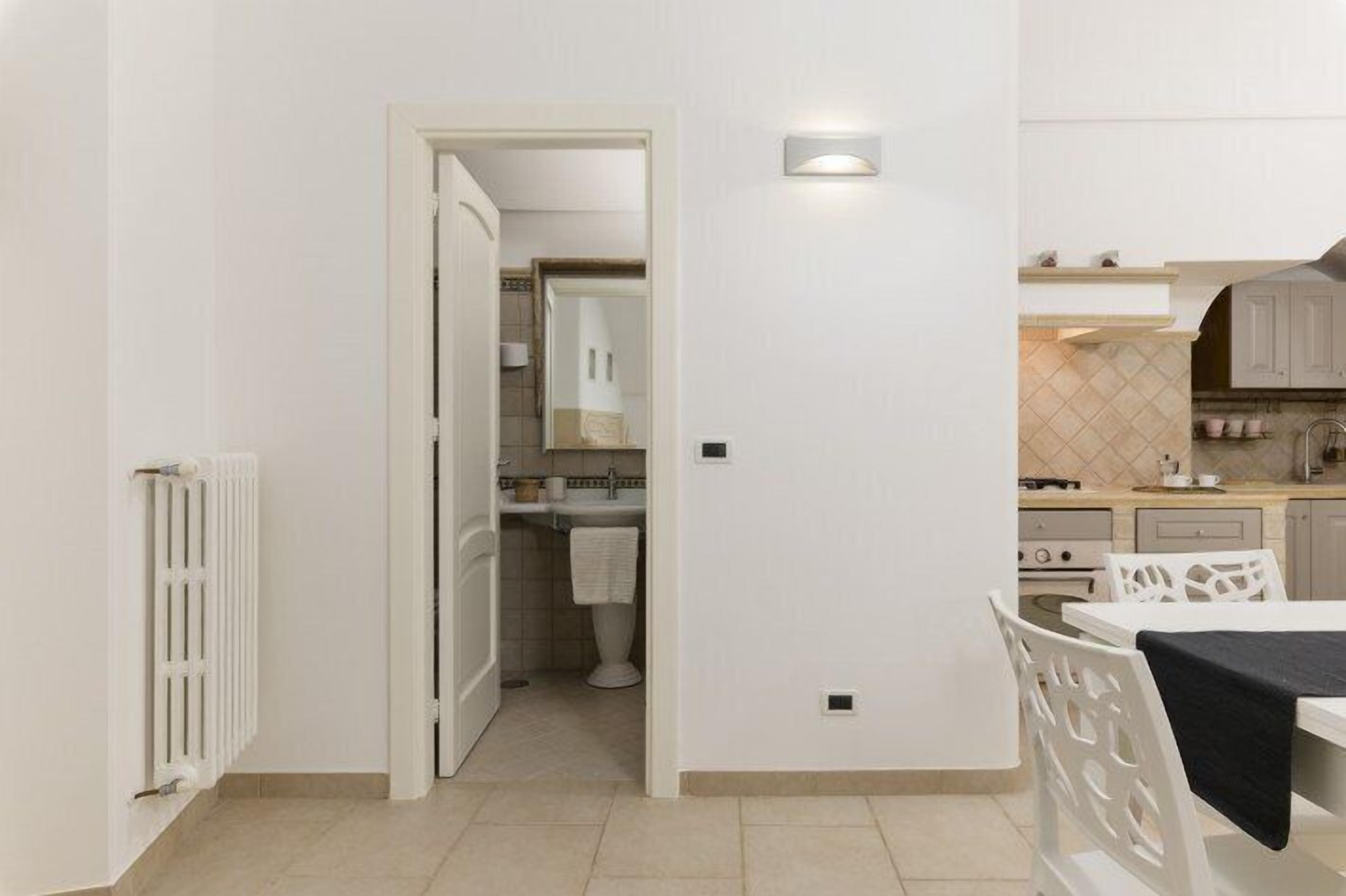 Une cuisine moderne avec des meubles blancs, un coin repas comprenant une table et des chaises, et une salle de bain visible avec des toilettes et un lavabo.