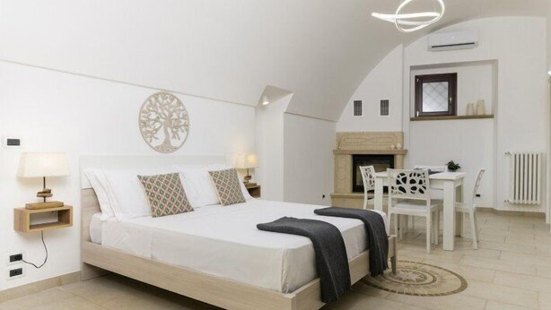 Een slaapkamer met een bed, nachtkastjes, een lamp, een open haard en een zithoek met stoelen.