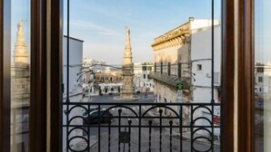 Uitzicht vanuit een raam op een stadsplein met historische gebouwen en een monument.