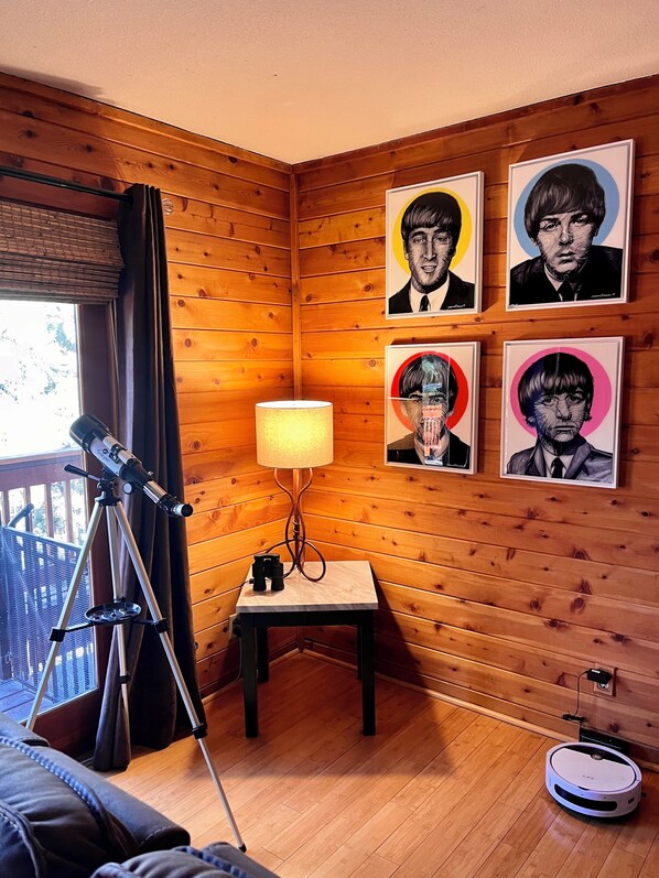 Una habitación con paneles de madera, un telescopio, una mesa con lámpara y retratos enmarcados en la pared.