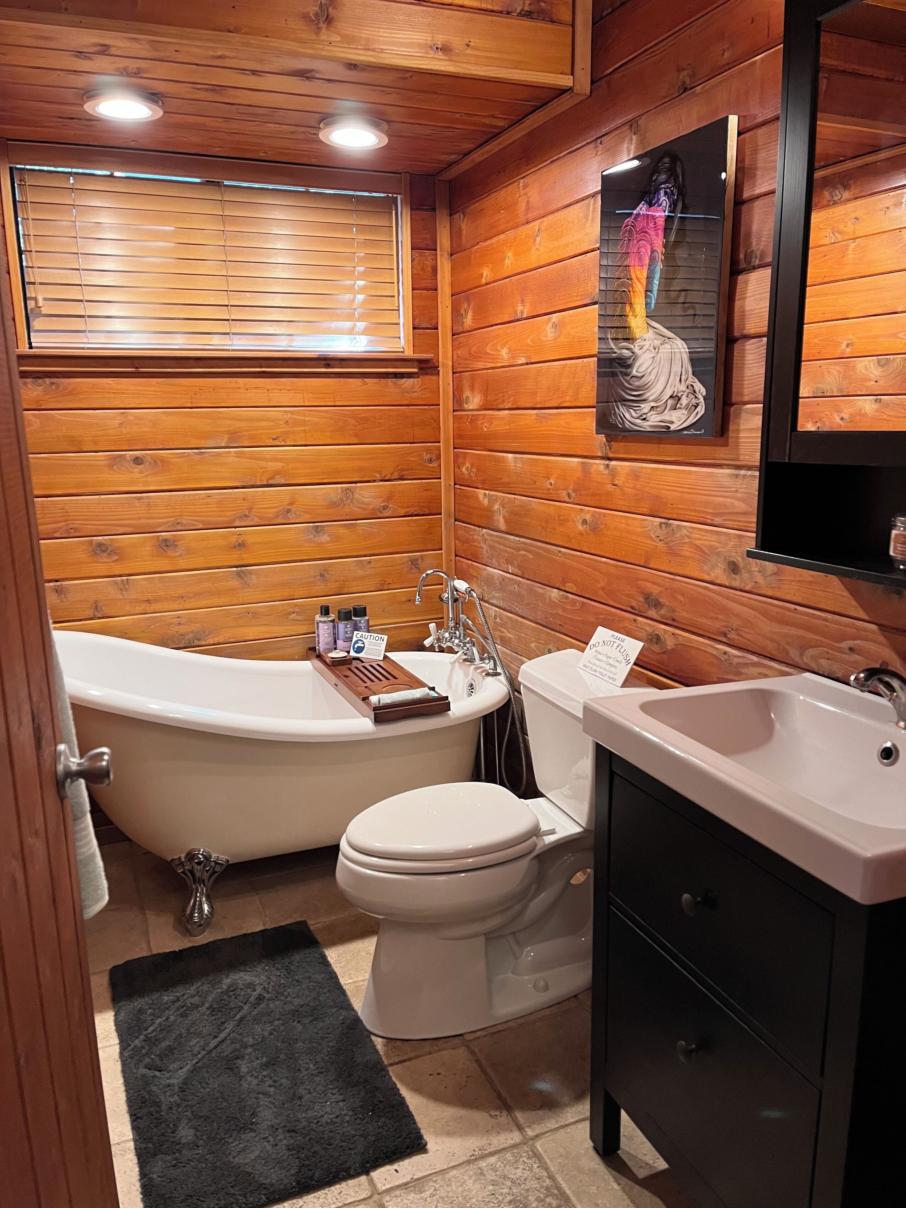Et badeværelse med træpaneler, badekar, toilet, håndvask og et håndklædestativ.