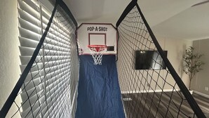 A basketball hoop with a sign reading "POP-A-SHOT" in a hallway with a blue mat on the floor, surrounded by a chain-link fence.