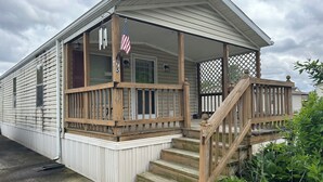 A single-story wooden house with a covered porch, a small staircase, and an American flag.