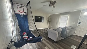 A living room with a basketball hoop, a couch, a TV, and a ceiling fan.