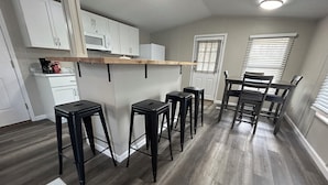A kitchen with white cabinets, a wooden bar counter, black stools, and a dining area with a table and chairs.