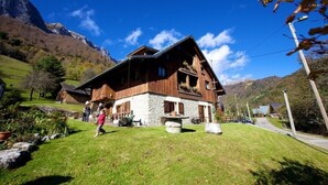 A wooden chalet with stone walls, a stone bench, and a mountain backdrop. - Apartment 'Les Lutins' with Mountain View, Shared Terrace and Wi-Fi (Saint-Ferréol)