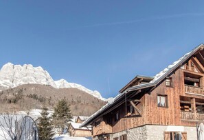 Un chalet de madera con cimientos de piedra, un balcón y vistas a montañas nevadas.
