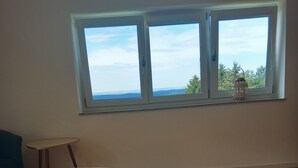 A bedroom with a large window, a wooden floor, and a bed with grey bedding. - Traumhaftes neu Renoviertes Apartment mit Herrlichem Ausblick & top Ausstattung (Lalling)